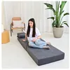 A young woman is sitting on a folded mattress in a room with a plant and a chair. Podgląd zdjęcia produktu