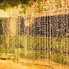 A curtain of fairy lights hanging outdoors at night, with greenery in the background. Náhled obrázku produktu
