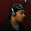 A man wearing headphones and a beanie against a brick wall. Produktbild-Vorschau