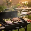 A person is grilling sausages and vegetables on a BBQ grill in a backyard setting. Podgląd zdjęcia produktu