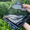 A person is holding a folded black and transparent tarp in front of a green leafy background. Náhled obrázku produktu