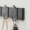 A close-up shot of a black wooden wall-mounted coat rack with multiple hooks, holding a handbag and keys. Produktbild-Vorschau