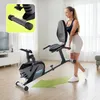 A woman is standing next to a stationary bike in a living room. Produktbild-Vorschau
