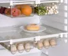 Inside a refrigerator, showing clear plastic storage drawers filled with food items like fruits, vegetables, and eggs, and a donut on a plate. Náhled obrázku produktu