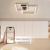 A hand holding a smartphone displaying a ceiling light, with the actual ceiling light visible above a kitchen cabinet. Voir les images du produit