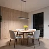 A modern dining room with a round wooden table, chairs, and a linear pendant light. Produktbild-Vorschau
