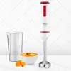 A white and red Ufesa hand blender with a stainless steel base, a clear measuring cup, a bowl of orange soup, and some chopped pumpkin pieces, set against a white tiled background. Voir les images du produit
