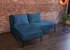 A blue sectional sofa is shown in a room with a brick wall and wooden floor. Produktbild-Vorschau