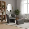A dark gray armchair and ottoman are placed on a rug in a living room setting, next to a bookshelf and a window with sheer curtains. Produktbild-Vorschau