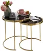 A set of two nesting tables with black glass tops and gold metal frames, decorated with a vase of pink flowers, a teacup, and a muffin. Produktbild-Vorschau