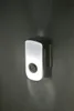 A white plug-in night light with a circular sensor in the center, mounted on a textured gray wall. Produktbild-Vorschau