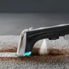 A close-up shot of a carpet cleaner spraying water onto a stained carpet. Voir les images du produit