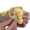 A hand holding a small yellow toy bear with a yellow chain attached. Anteprima dell’immagine prodotto