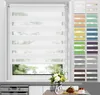 A white dual-layer roller blind is shown in a window, with a selection of color swatches for the blind on the right side of the image. A vase of flowers and a pastry are visible on a countertop below the window. Produktbild-Vorschau