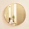 A round mirror with a gold frame hanging on a wall. Produktbild-Vorschau