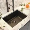 A black kitchen faucet with a pull-out spray is shown installed in a sink with a marble countertop. A glass of amber liquid with a honey dipper is placed on the counter nearby, along with some greenery. Podgląd zdjęcia produktu