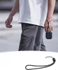 A person walking outdoors, holding a small black square device with a lanyard attached to their wrist. Anteprima dell’immagine prodotto