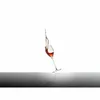 A wine glass with red wine splashing out of it, set against a white background with a reflective surface below. Podgląd zdjęcia produktu