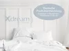 A white bed with rumpled white sheets and pillows, set against a white paneled headboard. A blue oval overlay with text is present in the upper right corner. Produktbild-Vorschau