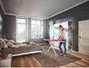 A woman is ironing clothes on an ironing board in a bedroom. Produktbild-Vorschau
