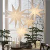 A festive indoor scene with paper star lanterns hanging in front of a window with a snowy view, surrounded by small Christmas trees and candles. Podgląd zdjęcia produktu