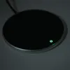 A close-up, slightly angled view of a round, black object with a silver rim, resting on a gray surface. A small green light is illuminated on the surface of the object. Podgląd zdjęcia produktu