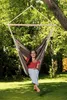 A woman sits in a hammock chair hanging from a tree in a grassy yard. Produktbild-Vorschau