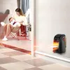 A woman holding a baby sits in a chair while a small heater is plugged into the wall and blowing warm air. Anteprima dell’immagine prodotto