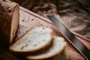 A close-up shot of sliced bread on a wooden cutting board next to a serrated knife. Voir les images du produit