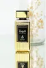 A gold perfume bottle with a black label, displayed on a reflective surface with a blurred background. Produktbild-Vorschau