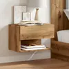 A wooden nightstand is mounted on a white wall next to a bed. The nightstand has a drawer on top and an open shelf below, with books and artwork on display. Produktbild-Vorschau