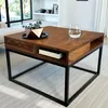 A square wooden coffee table with a black metal frame, placed in a living room setting. Produktbild-Vorschau