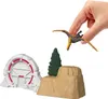 A hand holding a toy pterodactyl above a miniature Jurassic World scene with a gate and rocky terrain. Produktbild-Vorschau