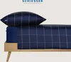 A close-up view of a dark blue checkered pillow and duvet on a wooden bed frame. Produktbild-Vorschau