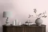 A decorative vignette on a wooden cabinet, featuring a lamp, candles, a bowl with pears, and a vase with branches against a pink wall. Produktbild-Vorschau