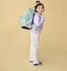 A young girl is wearing a backpack and standing against a plain background. Podgląd zdjęcia produktu