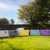 Five colorful lounge sofas are arranged on a grassy lawn in front of a hedge and a tent. Produktbild-Vorschau