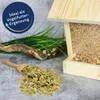 A wooden bird feeder filled with birdseed, with a pile of pea flakes and a wooden scoop in the foreground, and artificial grass and a piece of driftwood in the background. Produktbild-Vorschau