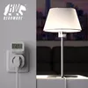 A close-up of a wall socket with a Bearware energy meter plugged in, and a lamp on a table in the background. Podgląd zdjęcia produktu