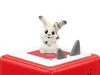A ceramic bunny figurine with Christmas lights sits on top of a red Toniebox. Produktbild-Vorschau