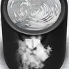 A close-up view of the top of a black electric kettle, showing steam rising from the spout and a distorted reflection in the water inside. Produktbild-Vorschau
