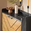 A close-up view of a modern shoe cabinet with a black top and wooden chevron-patterned doors. Produktbild-Vorschau
