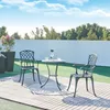 An outdoor patio setting with a bistro set, plants, and a white wall.