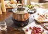 A copper fondue pot set is displayed on a table with ingredients for fondue. Podgląd zdjęcia produktu