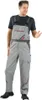A man wearing gray overalls with red accents and a black t-shirt, standing against a white background. Produktbild-Vorschau