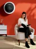 A woman sits in a chair reading a book next to a small washing machine mounted on the wall. Produktbild-Vorschau