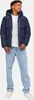 A young boy is posing for a product shot, wearing a navy puffer jacket and light blue jeans. Produktbild-Vorschau