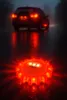 A red LED warning light is placed on a wet road at night, with a car's taillights visible in the background. Podgląd zdjęcia produktu