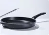 A black frying pan with a silver handle is shown on a white surface against a white background. Náhled obrázku produktu