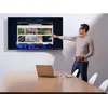 A man is pointing at a large screen displaying a web browser with multiple images, while a laptop sits on a table in front of him. Produktbild-Vorschau